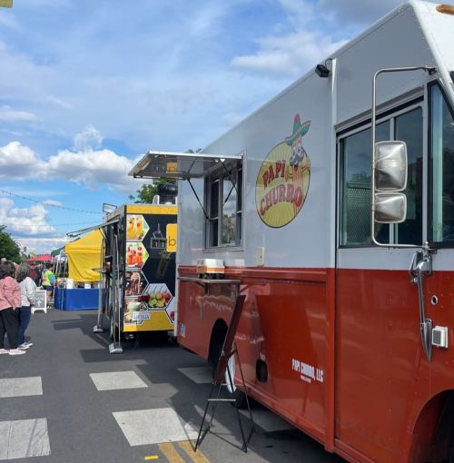 Two food trucks parked at an outdoor event, one with a colorful sign reading "Papi Churro." People are nearby.
