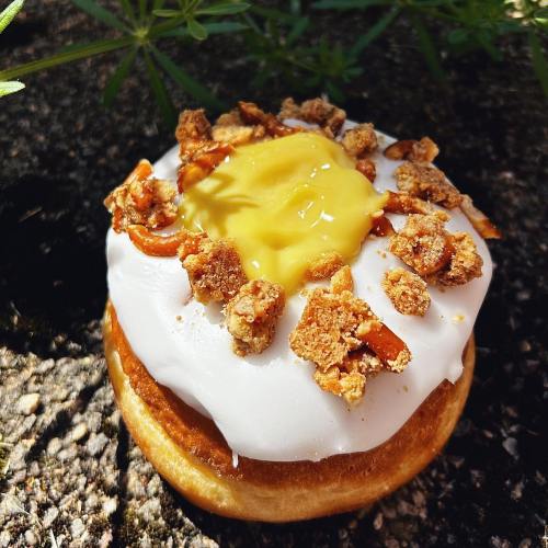 A glazed donut topped with yellow custard and crunchy bits, set against a natural background.