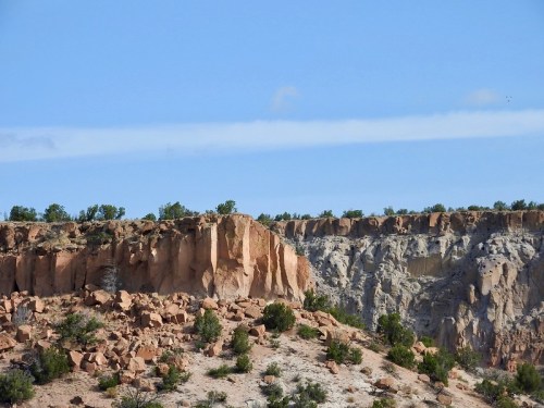 A rocky cliff with layered formations and sparse vegetation under a clear blue sky.
