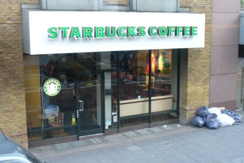 Exterior view of a Starbucks Coffee shop with a green sign, large windows, and garbage bags nearby.