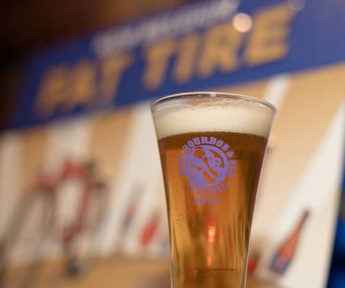 A glass of beer with a logo for the Bourbon & BBQ Festival 2018 in the background.
