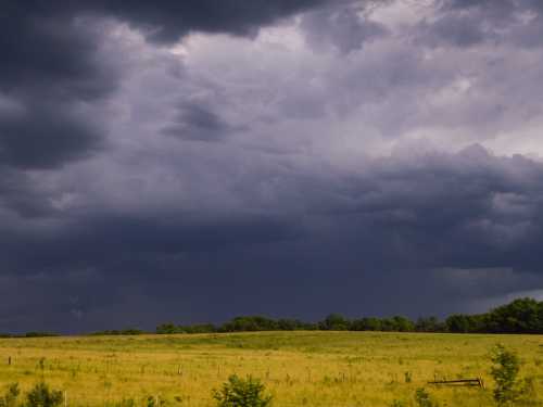 A vast grassy field under a dramatic sky filled with dark, looming clouds.