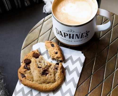 A latte in a mug beside a chocolate chip cookie on a chevron-patterned napkin.