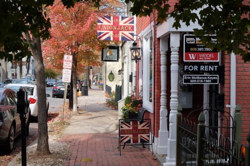A charming street scene featuring a British-themed pub sign, autumn leaves, and storefronts in a quaint neighborhood.