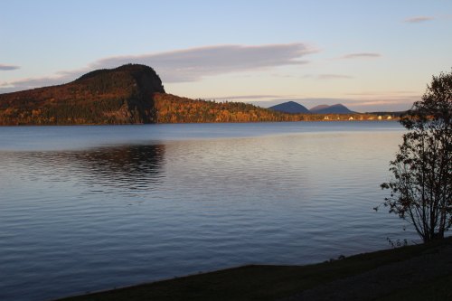 A serene lake at sunset, reflecting mountains and colorful autumn foliage under a clear sky.