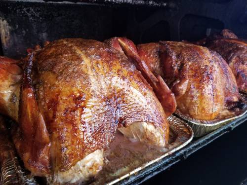 Two golden-brown roasted turkeys in metal trays, glistening with seasoning and juices, inside a smoker.