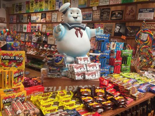 A colorful candy shop display featuring a Stay Puft Marshmallow Man statue surrounded by various candy brands.