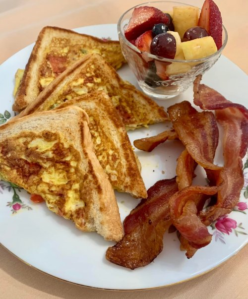 A plate with French toast, crispy bacon, and a fruit cup with strawberries, grapes, and pineapple.