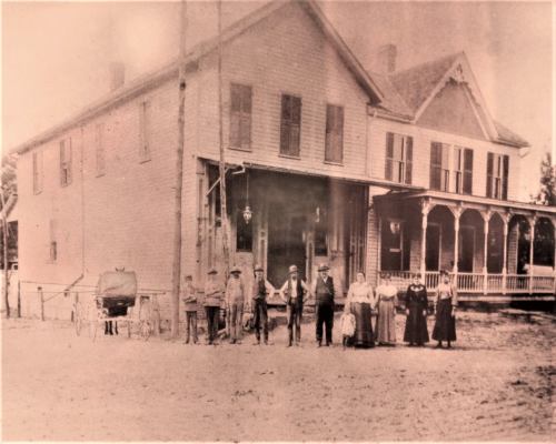 A historic black-and-white photo of a group of people standing in front of a large house, with a horse-drawn carriage nearby.