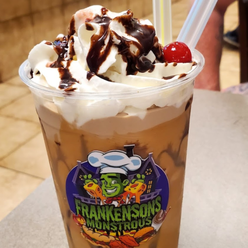 A delicious dessert drink topped with whipped cream, chocolate syrup, and a cherry, served in a branded cup.