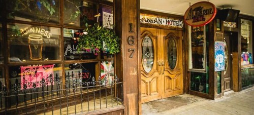 Exterior of a pub with wooden doors, large windows displaying drinks, and colorful signage.