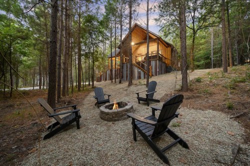 A cozy cabin in the woods with a fire pit and seating area surrounded by trees.