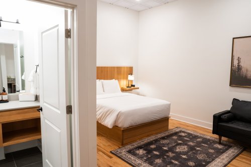 A modern hotel room featuring a bed, a black sofa, and a bathroom area with a mirror and sink.