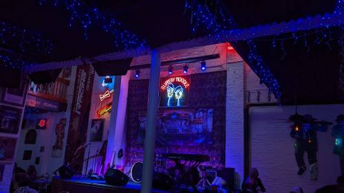 A vibrant music venue with colorful lights, a stage, and a neon sign reading "Supper Club" in the background.