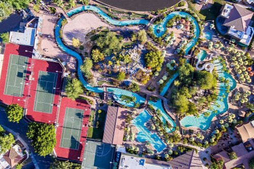 Aerial view of a resort featuring winding pools, lush landscaping, and tennis courts nearby.