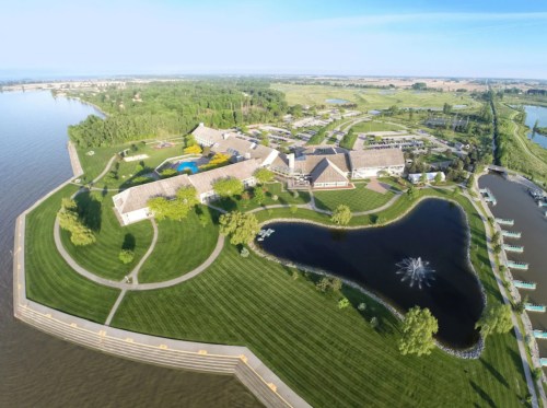 Aerial view of a large resort with landscaped grounds, a pond, and a river nearby, surrounded by greenery.