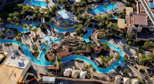 Aerial view of a resort pool area featuring winding water slides, palm trees, and multiple swimming pools.
