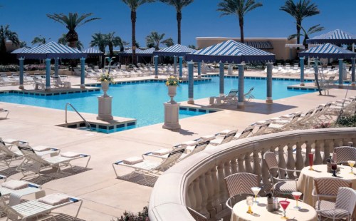 A sunny pool area with blue-striped cabanas, lounge chairs, and palm trees, creating a relaxing atmosphere.