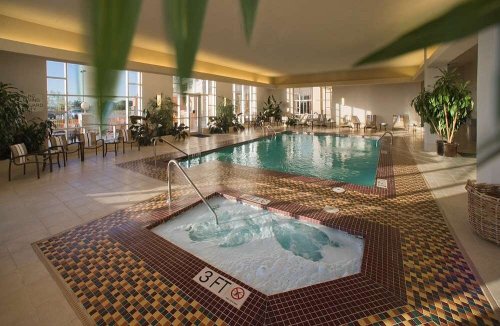 Indoor pool area featuring a swimming pool and a hot tub, surrounded by plants and lounge chairs.