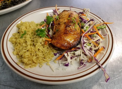A plate featuring grilled chicken, yellow rice, and a colorful cabbage salad with carrots and herbs.