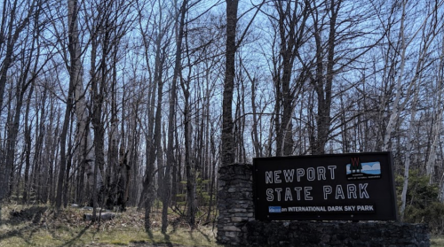 Sign for Newport State Park surrounded by bare trees and a clear blue sky, indicating it's an International Dark Sky Park.