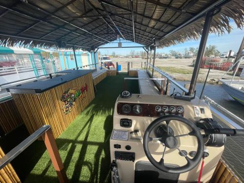 Interior of a boat with a thatched roof, featuring a steering console and green turf flooring.