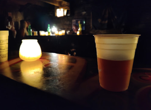 A dimly lit bar scene featuring a plastic cup of beer and a glowing candle on the counter.
