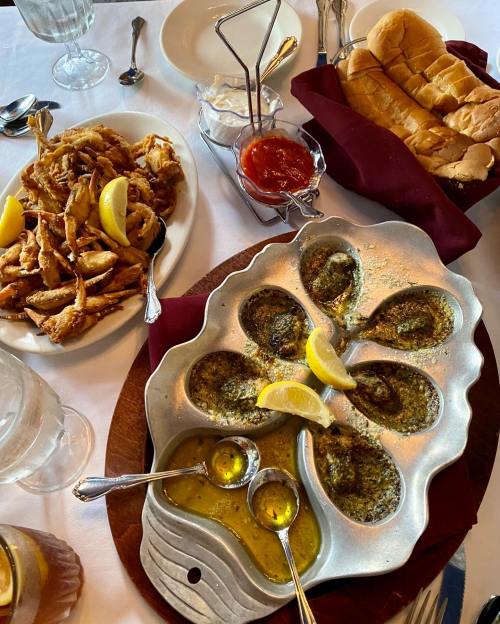 A table spread featuring fried seafood, baked oysters with lemon, and a basket of bread, all elegantly arranged.