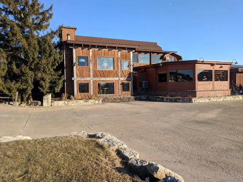 A rustic wooden building with large windows and a stone border, set against a clear blue sky.
