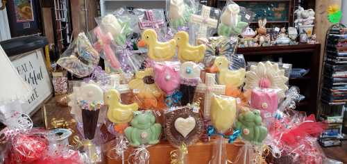 A colorful display of decorative chocolate treats, including ducks, flowers, and frogs, arranged in a shop.