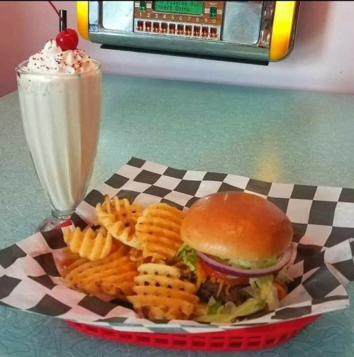 A classic diner meal featuring a burger, waffle fries, and a milkshake topped with whipped cream and a cherry.