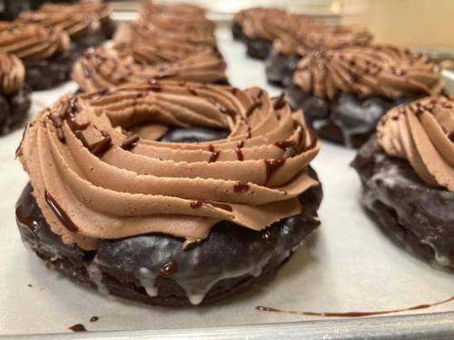 A close-up of chocolate frosted donuts with swirls of chocolate icing and a drizzle of chocolate sauce on top.