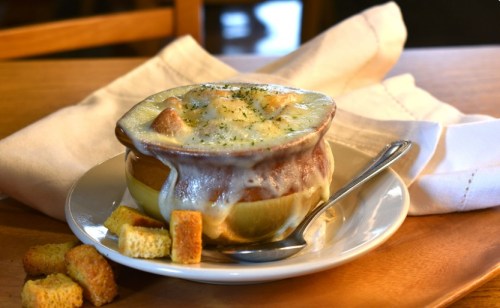 A bowl of French onion soup topped with melted cheese, served with croutons on the side.