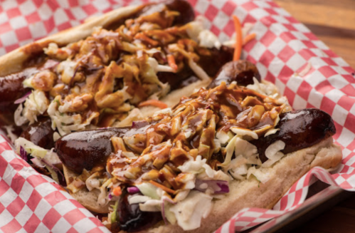 Two hot dogs topped with coleslaw and drizzled with sauce, served in a red and white checkered basket.