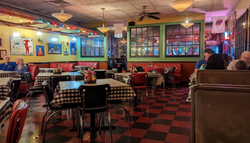 A cozy diner with checkered tablecloths, colorful lights, and patrons enjoying their meals in a vibrant atmosphere.