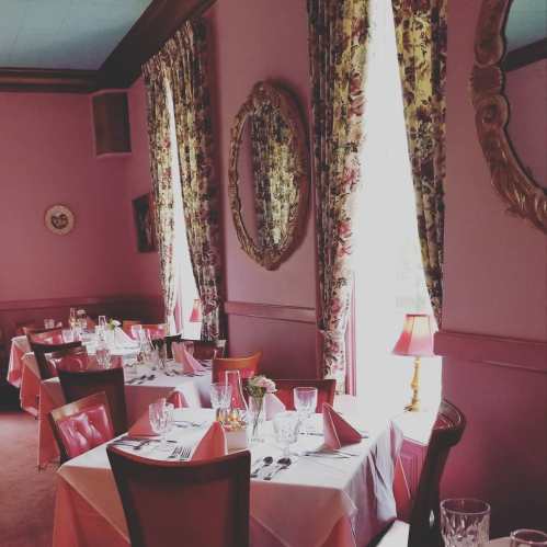 Elegant dining room with pink walls, floral curtains, and neatly set tables with glassware and napkins.