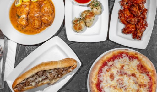 A spread of delicious dishes including chicken, scallops, wings, a sub, and pizza on a table.