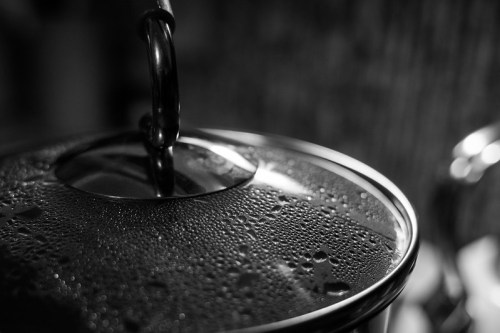 Close-up of a metallic pot lid with condensation droplets, set against a blurred background in black and white.