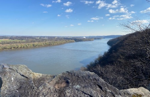 A scenic view of a river winding through green hills under a clear blue sky with scattered clouds.