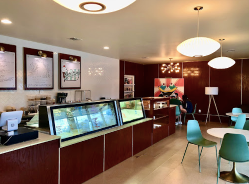 A modern café interior with a service counter, menu boards, and seating area featuring green chairs and stylish lighting.