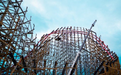 A partially constructed wooden roller coaster against a cloudy sky, showcasing its intricate framework and structure.