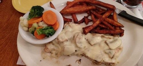 A plate with grilled chicken topped with cheese and mushrooms, served with sweet potato fries and a side of mixed vegetables.