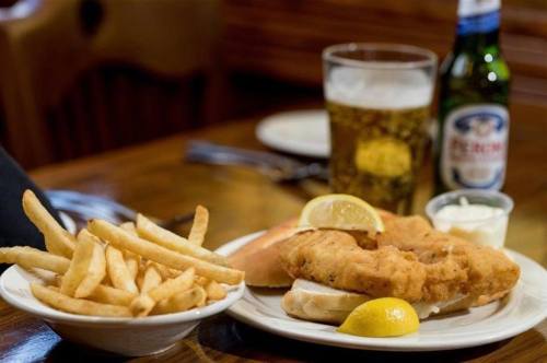 A plate of fried fish with lemon, served with fries and a side of dipping sauce, alongside a glass of beer.