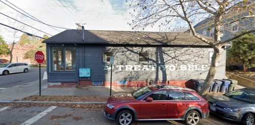 A gray building with "Treat Yo Self" painted on the side, parked cars, and a stop sign nearby.