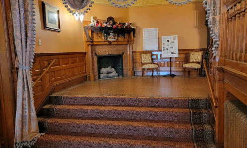 A staircase leading to a cozy room with a fireplace, decorated with chairs and festive decor.