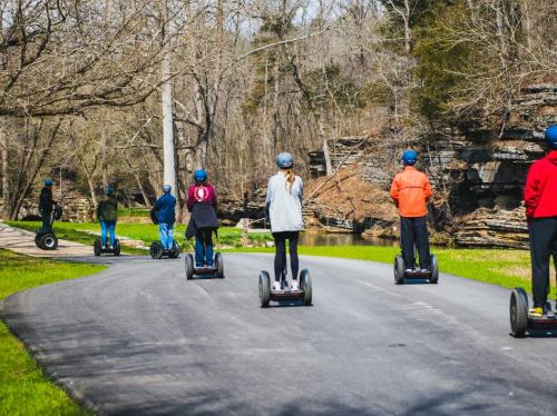 A group of people riding segways along a scenic path with trees and rocks in the background.
