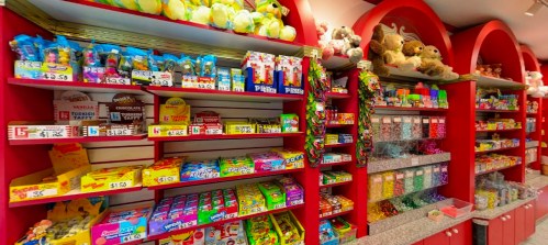 Colorful candy shop shelves filled with various candies, toys, and stuffed animals in a vibrant, inviting display.