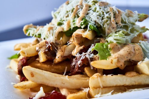 A close-up of loaded fries topped with lettuce, cheese, and a creamy sauce, served on a white plate.