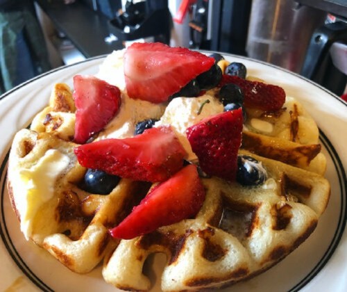 A golden waffle topped with strawberries, blueberries, and a scoop of ice cream, served on a white plate.