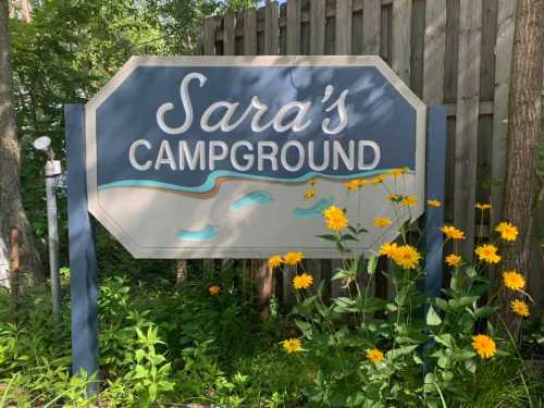 Sign for "Sara's Campground" surrounded by yellow flowers and greenery.